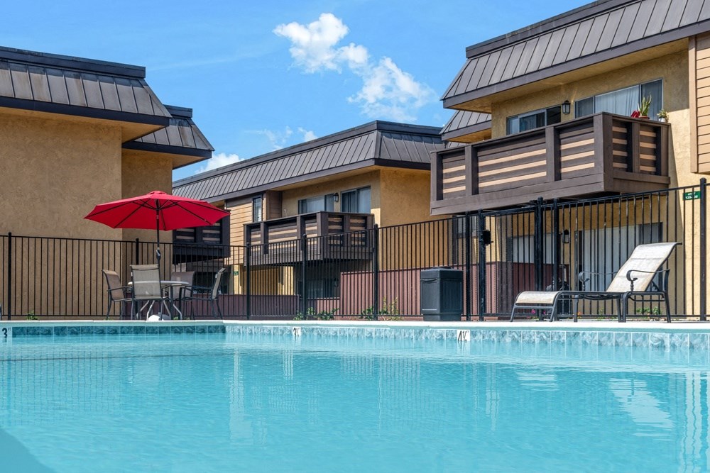 A red umbrella is on the left side of a pool.
