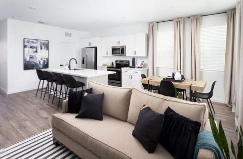 A living room with a couch, chairs, and a kitchen area in the background.