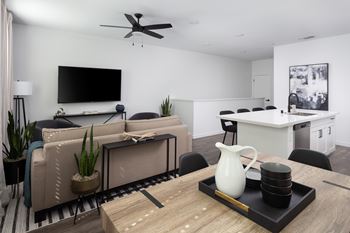 A modern living room with a flat screen TV, a sofa set, a coffee table, and a kitchen area in the background.