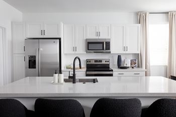 A kitchen with a white countertop and black chairs.