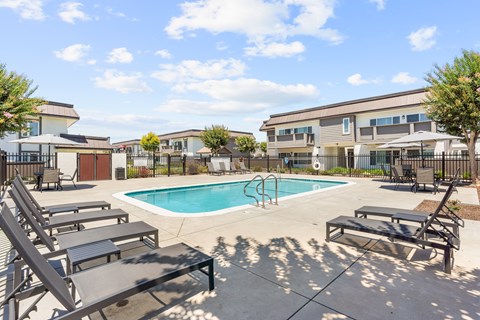A pool with sun loungers and a building in the background.