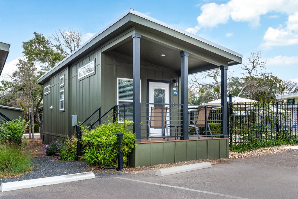 a green tiny house with a porch with two chairs on it