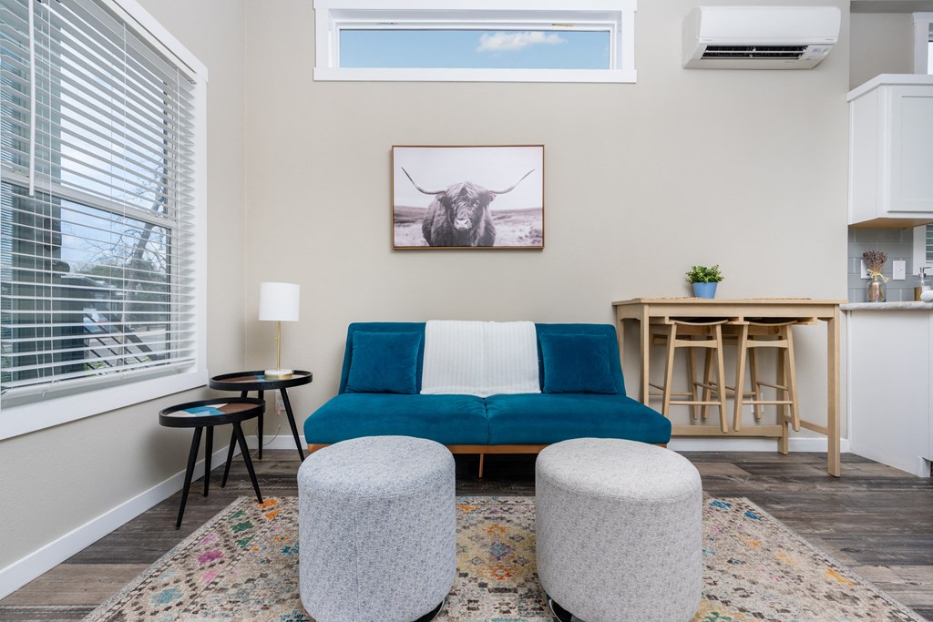 a living room with a blue couch and stools and a kitchen with a window