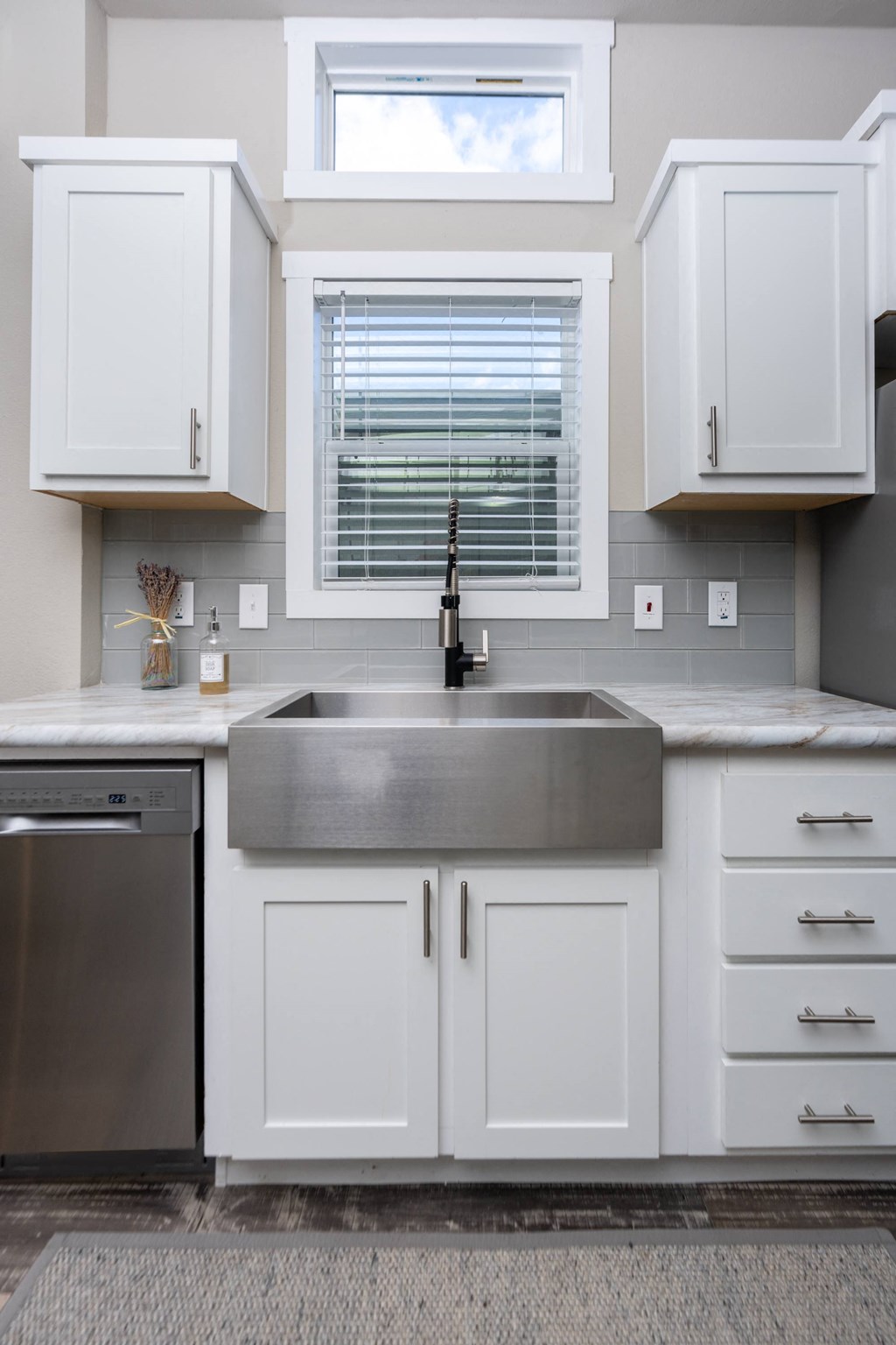 Apartments For Rent In South Austin, TX - Casata Austin - Kitchen With Stainless Steel Appliances, Farmhouse Sink, Wood-Inspired Plank Flooring, White Cabinets, And Window With Blinds