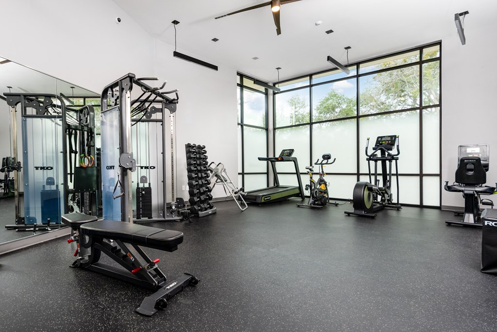 a gym with weights and cardio equipment and large windows