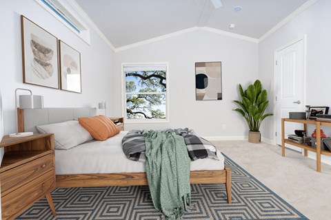 A bedroom with a bed, nightstand, and a window with a view of trees.