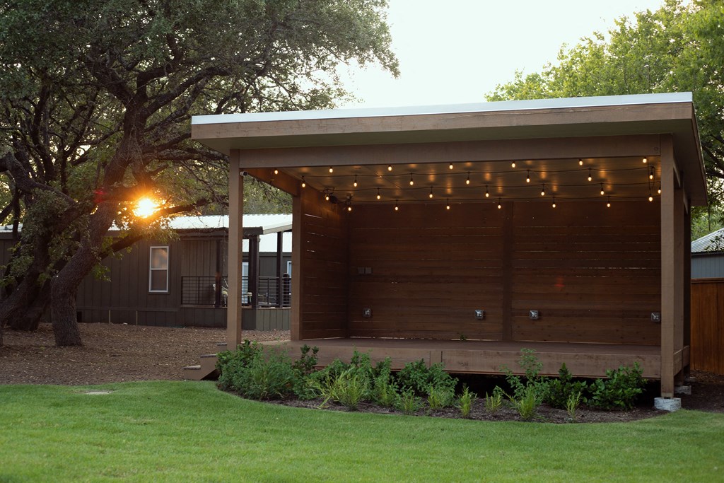 One And Two-BR Apartments In South Austin, TX - Casata Austin - Courtyard Covered In Trees With Two Benches, And Tavern Lighting.
