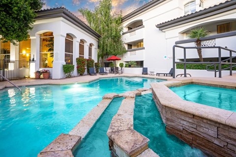 A swimming pool with a stone border and a building with a balcony in the background.
