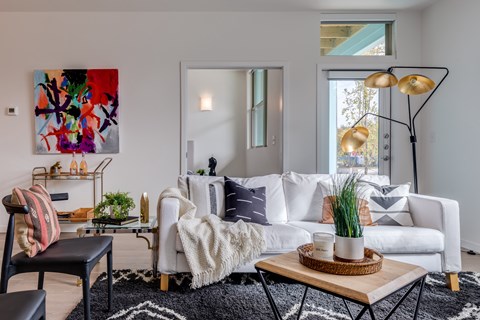 A living room with a white couch, a black chair, a coffee table, and a colorful painting on the wall.