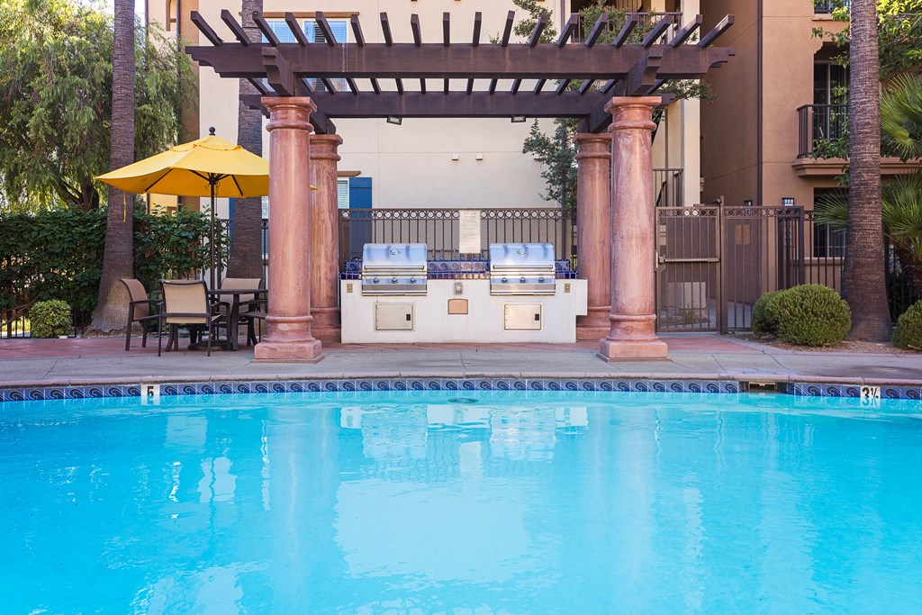 an outdoor kitchen next to a swimming pool with a hot tub and a pergola