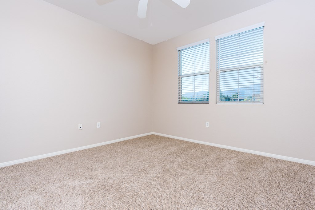 a bedroom with beige carpet and two windows