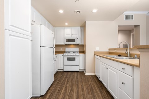 a kitchen with white cabinets and appliances and a wood floor
