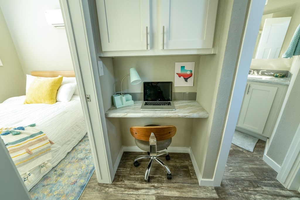 a small desk with a laptop and a desk chair in a room with a bed in model unit