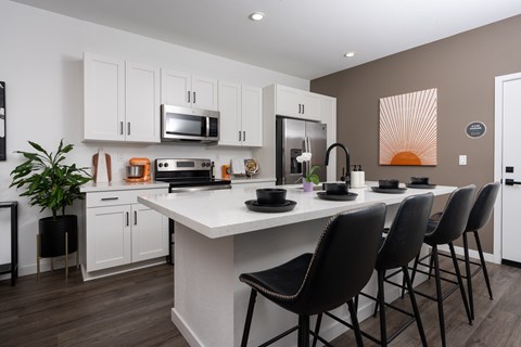 A modern kitchen with a white island and black chairs.