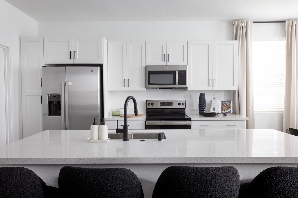a kitchen with white cabinets and a large white island with black chairs