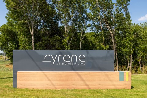 A sign that says "Cyrene at Painted Tree" is in front of a grassy area with trees in the background.