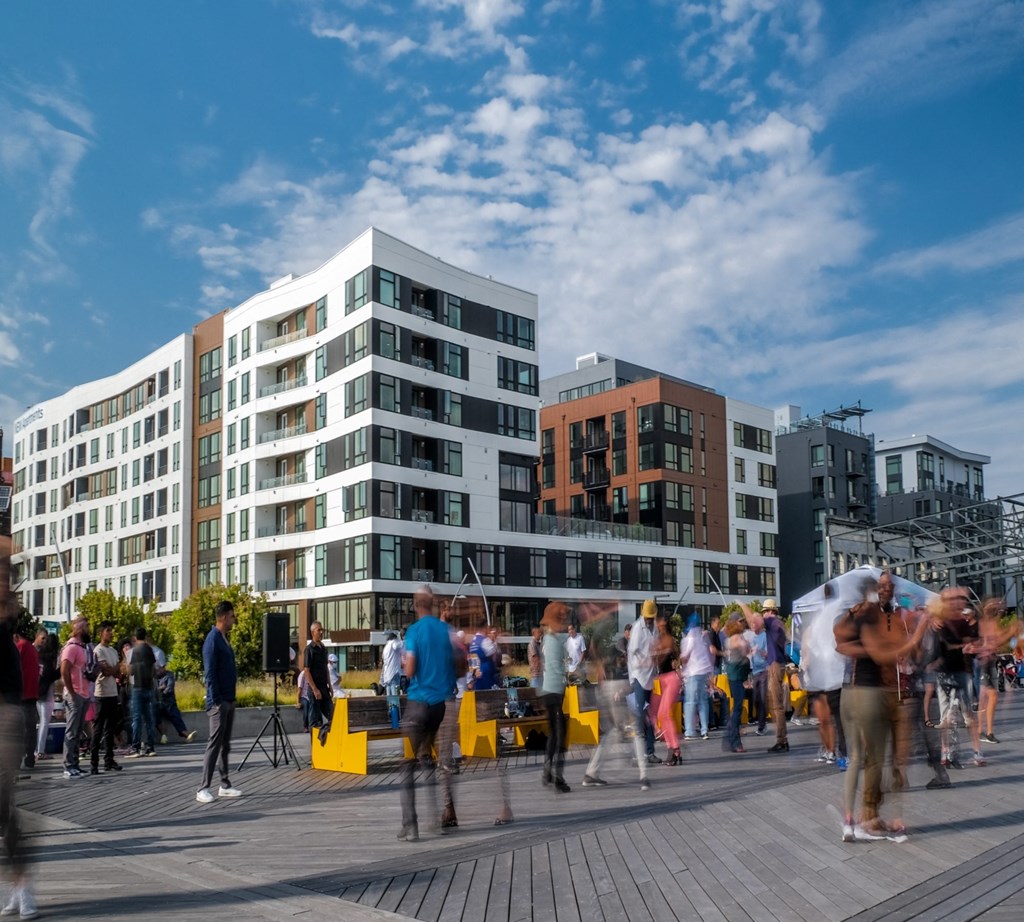 a crowd of people walking on a boardwalk in front of buildings