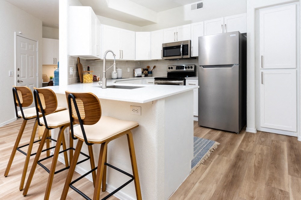 a kitchen with a large island with stools and a stainless steel refrigerator