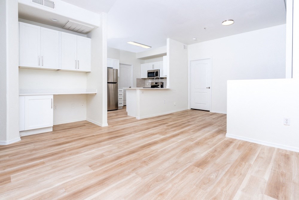 an empty living room with a wood floor and a kitchen