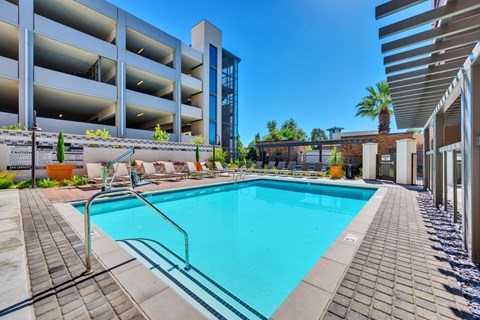 Dog-Friendly Luxury Apartments in Ontario, CA - Downtown Ontario Luxury Apartments - Swimming Pool With Lounge Seating, A Shaded Patio Area, And A Modern Apartment Building.