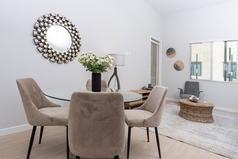 Two Bedroom Luxury Apartments in Ontario, CA - Downtown Ontario Luxury Apartments - Dining Area with Round Dining Table, Tan Chairs, Decorative Wall-Mounted Mirror, and Wood Grain Vinyl Flooring.