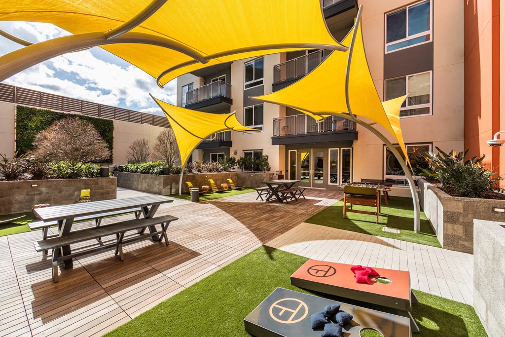 a courtyard with picnic tables and yellow umbrellas in front of an apartment building