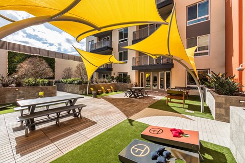 a courtyard with picnic tables and yellow umbrellas in front of an apartment building