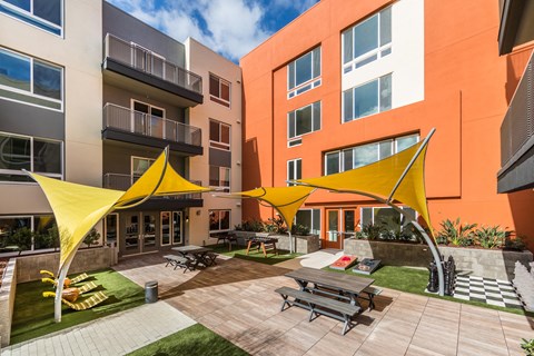 an outdoor courtyard of an apartment building with picnic tables and yellow umbrellas