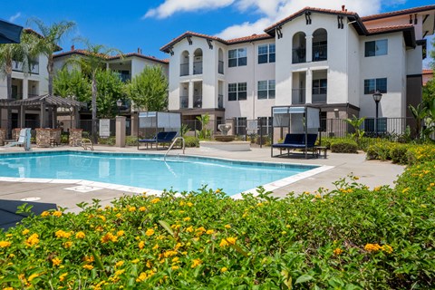 A pool surrounded by flowers and a building in the background. at 55+ FountainGlen Terra Vista, California, 91730