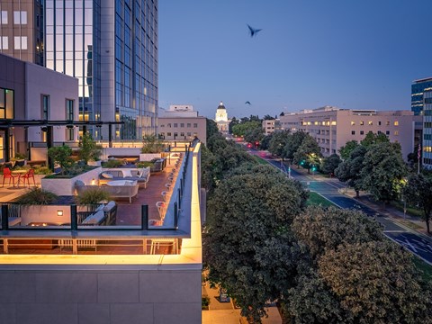 A bird flies over a city street at dusk.