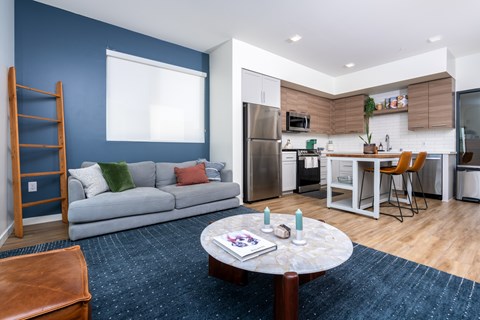 A modern kitchen with a dining table and chairs is adjacent to a living room with a sofa and a coffee table.