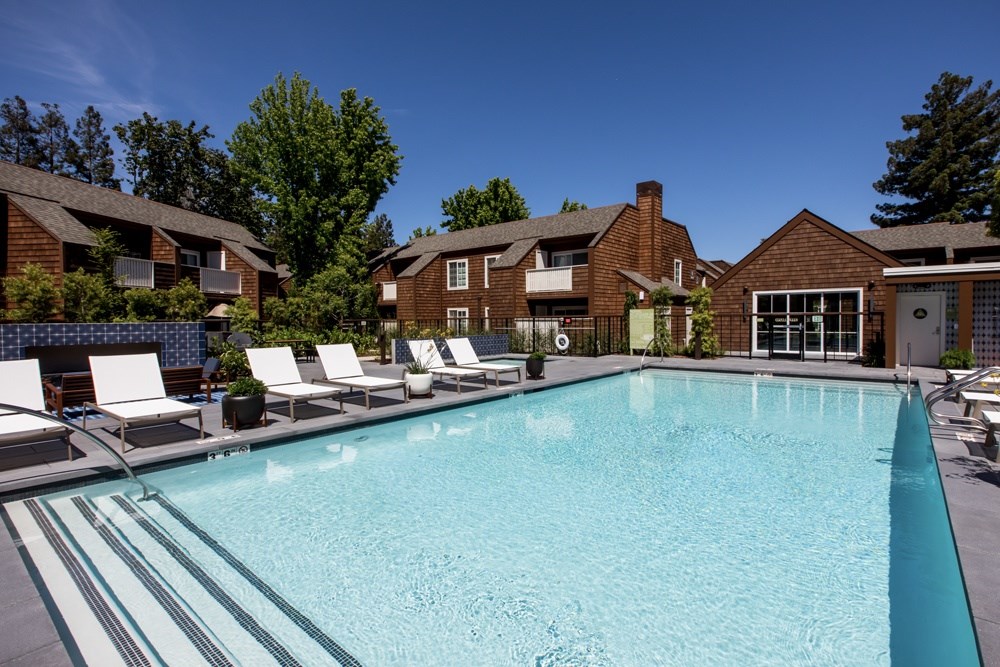 A large swimming pool surrounded by lounge chairs and buildings in the background.