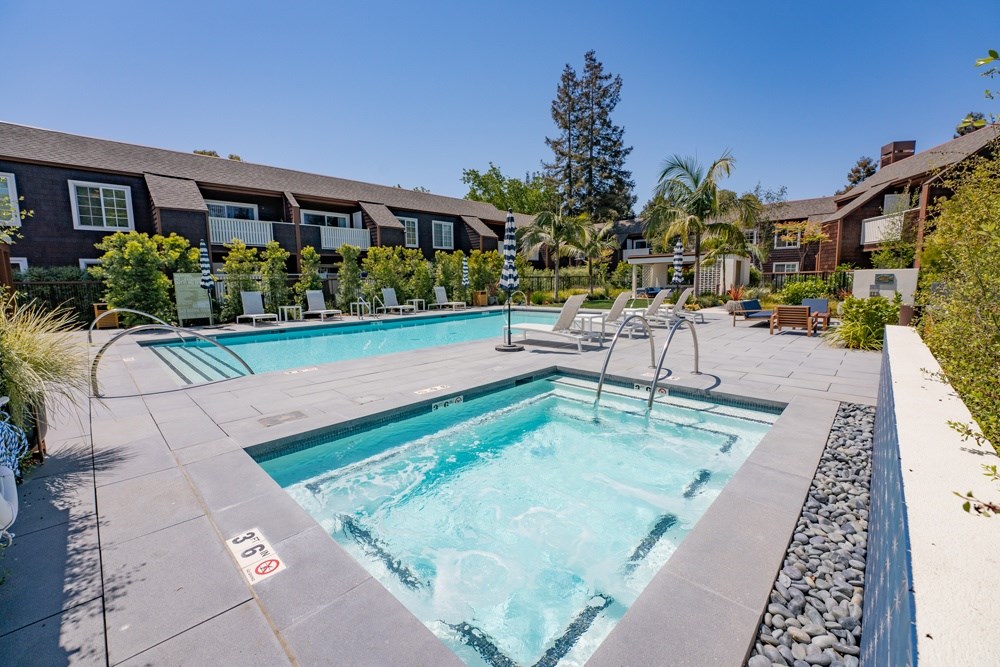 A swimming pool surrounded by a stone border and lounge chairs.