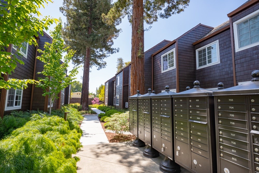 A row of mailboxes are on the sidewalk in front of a building.