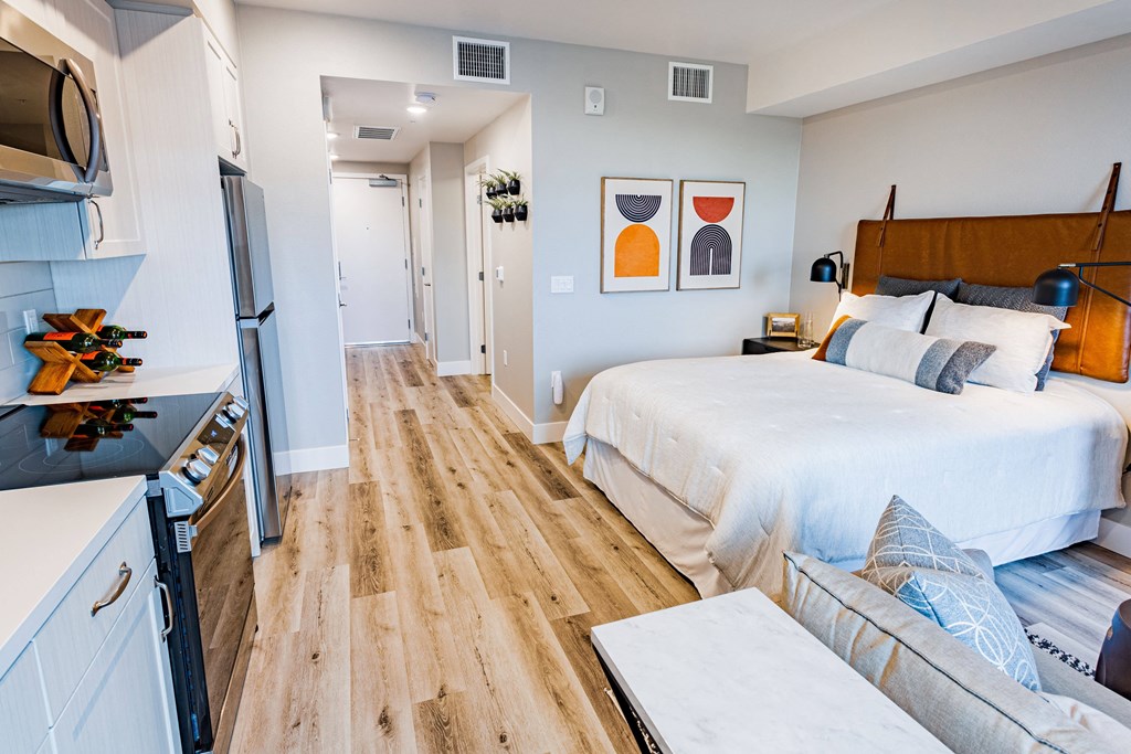 Studio apartment with bed, couch and white cabinets in kitchen area with a black stove top oven