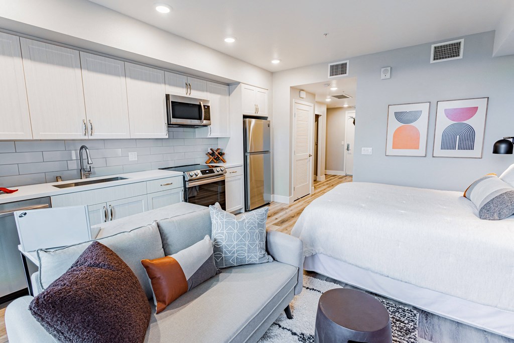 Studio apartment with bed, couch, stainless steal fridge and white cabinets