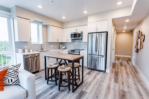 Sunnyvale, CA Pet-Friendly Apartments - 1250 Lakeside - Modern Kitchen With Stainless Steel Appliances, White Cabinets, Plank Style Flooring, And Island Table