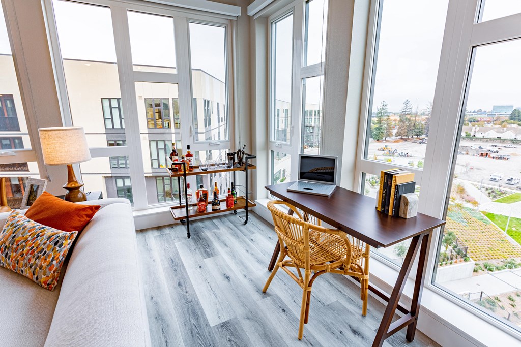 Livingroom with large windows, wood flooring and table with a chair.