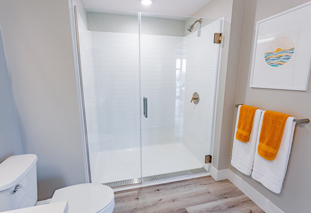 bathroom walk in shower with glass doors and white and orange towels on teh wall.