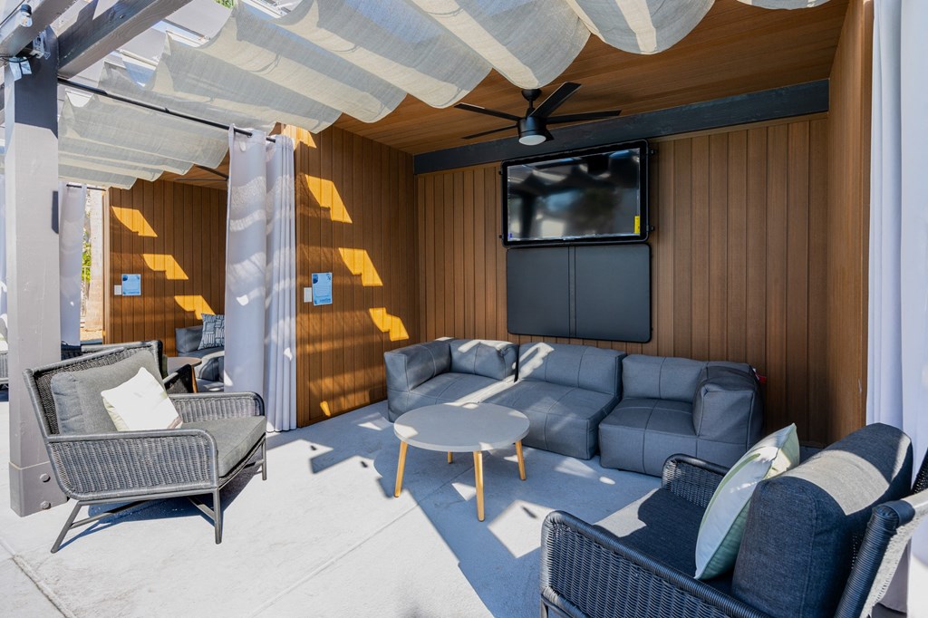 A patio with a grey sofa, a black chair and a white table at Verandas Apartments, West Covina, CA, 91791