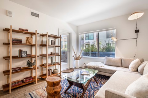 A living room with a white couch, a glass coffee table, and a bookshelf with books and decorative items.