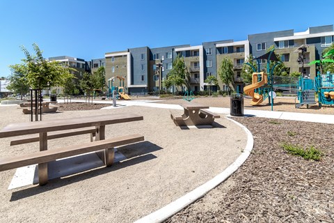 a park with benches and playground equipment in front of apartment buildings