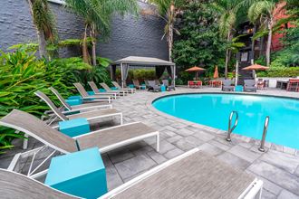 Apartments For Rent Downtown San Diego - Refreshing Pool And Lounge Area. Pool Is Surrounded By Lounge Chairs, Tables, Umbrellas, Canopy, And Tropical Lush Landscape.