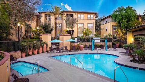 A swimming pool surrounded by a patio with chairs and a building in the background.