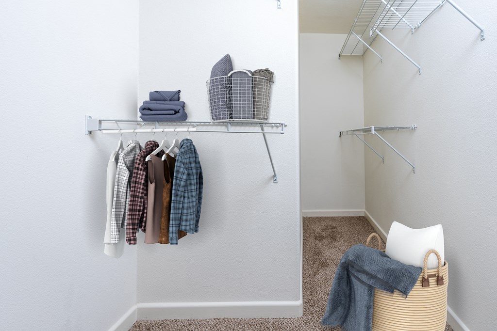 a walk in closet with clothes, a basket with blankets and items on a shelf.