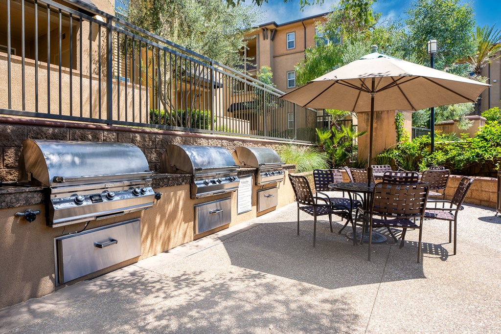 an outdoor patio with barbecue grills and a table with chairs and an umbrella