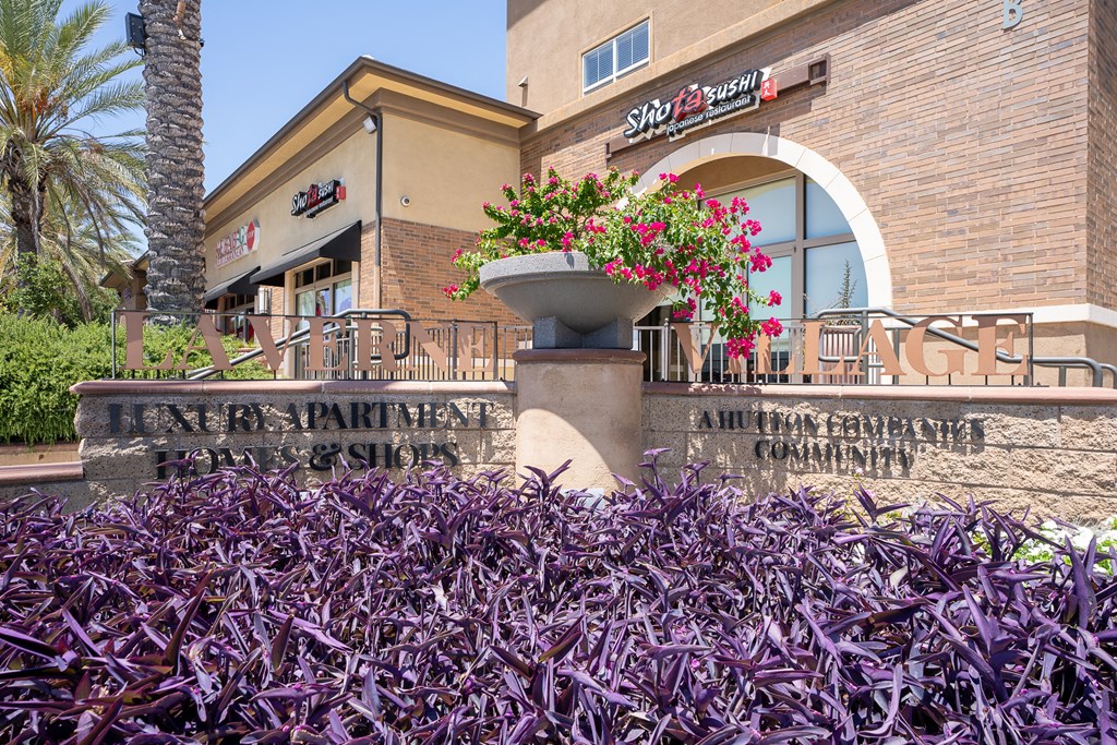 a building with a sign on it and purple plants in front of it