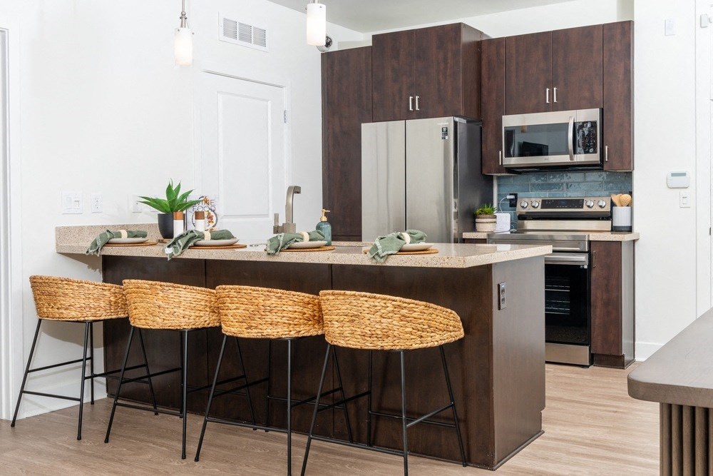 Apartments for Rent in Phoenix AZ - Level at Sixteenth - Modern Kitchen with Wood-Style Flooring, Dark Wood Cabinetry, Stainless Steel Appliances, Sandy Granite Countertops, Blue Tile Backsplash, Pendant Lights Over Breakfast Bar Area with Place Settings and Bar Chairs