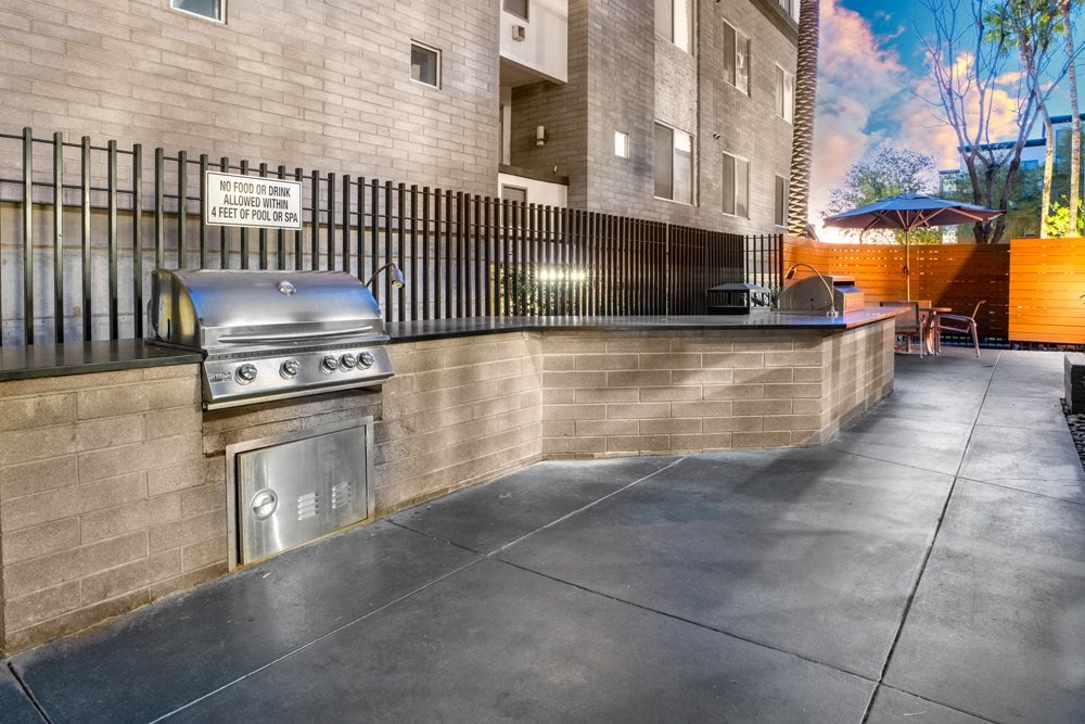 an outdoor patio with a grill and a bar with chairs and an umbrella