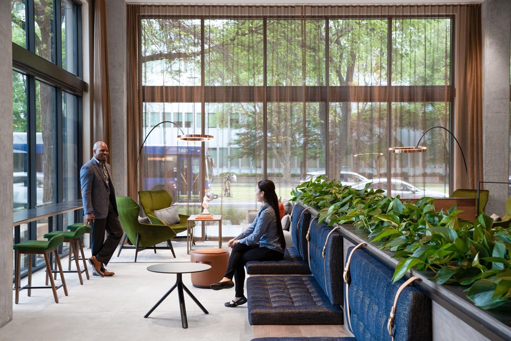 a man and woman walking through a lobby with chairs and plants